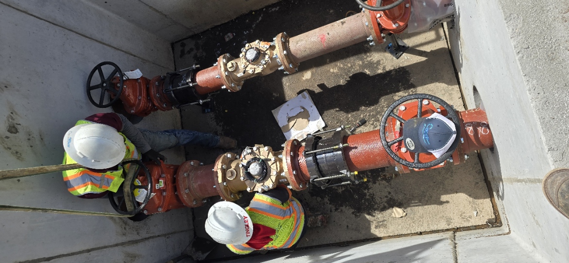 CMWC crew members in hard hats working on red and black pipe valves inside an underground vault