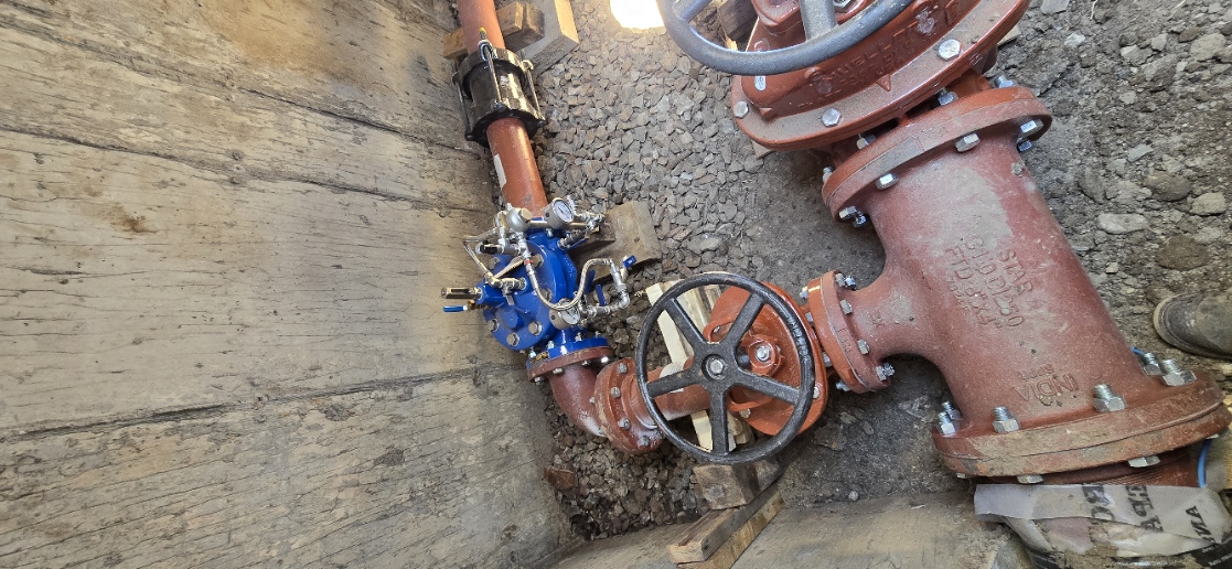 Close-up of a newly installed blue valve and red valve assembly in a gravel excavation
