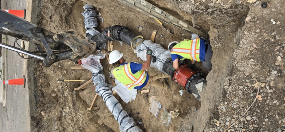 Workers in a trench connecting water main pipe sections during infrastructure replacement